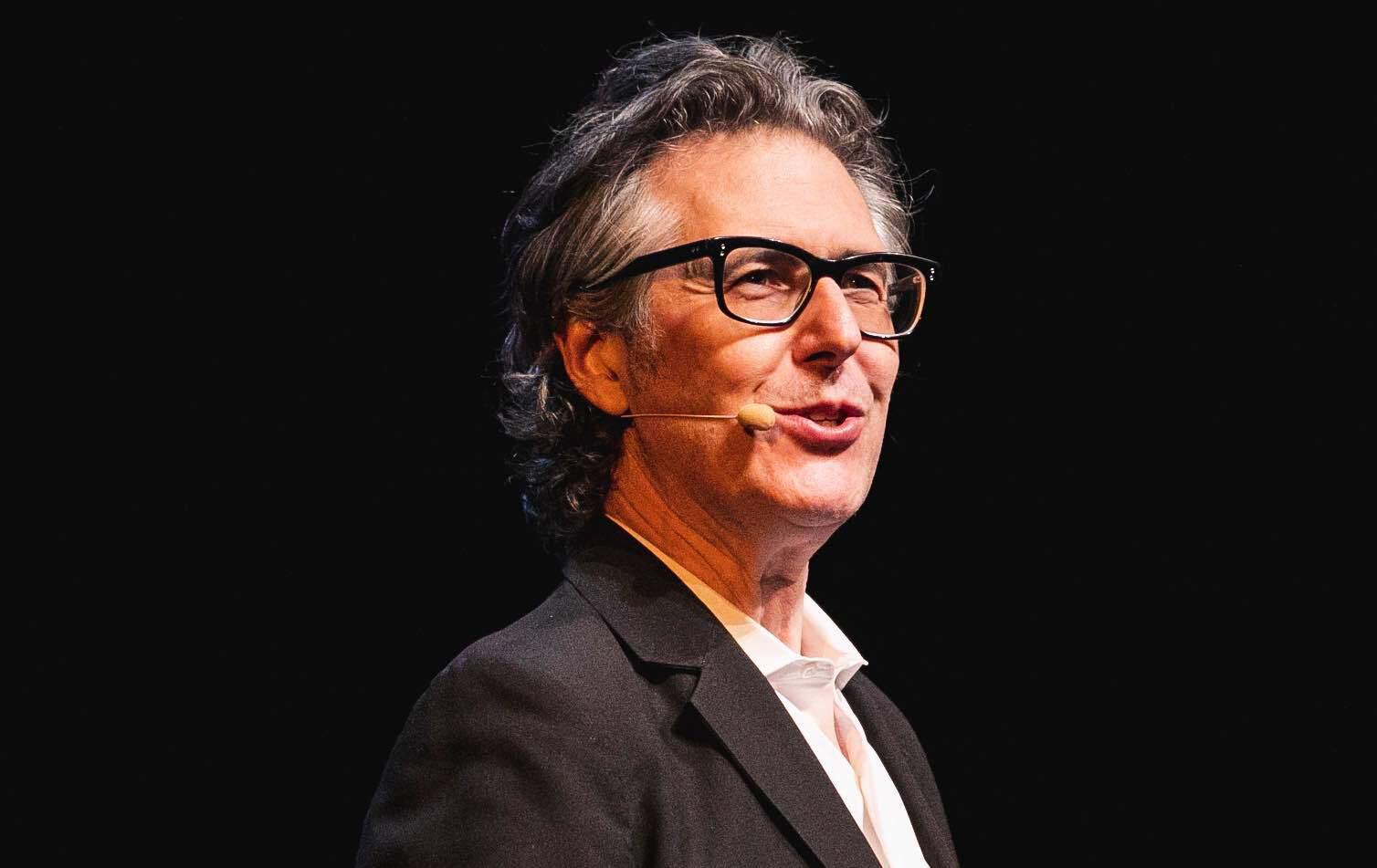 A photo of Ira Glass, on stage speaking in to a headset microphone.