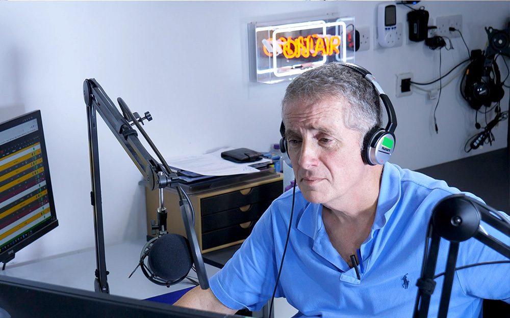 Image shows a man at a computer in a radio studio.
