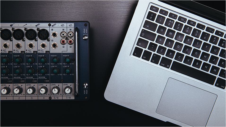 This is a mahogany dark desk. On the left is a mixing desk in black. On the right is a Silver and black Macbook keyboard and mouse set.