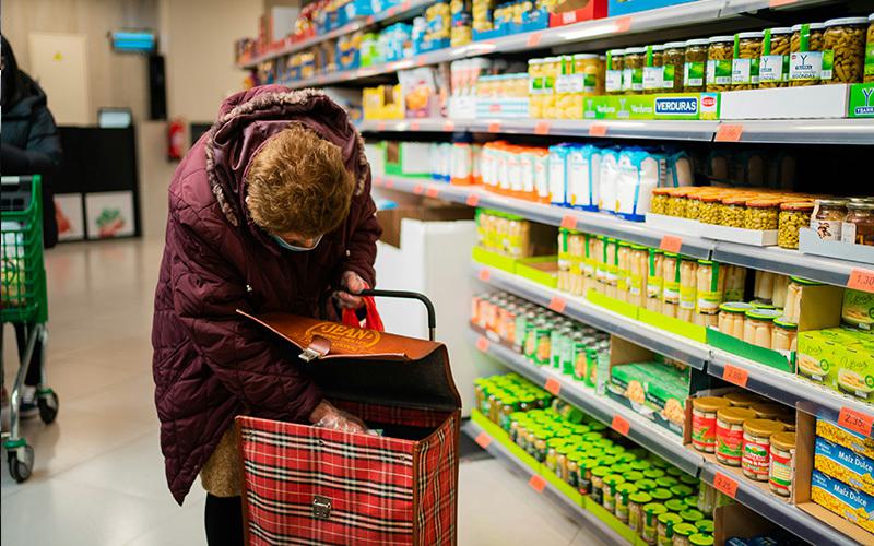 Image shows an older woman in a grocery store placing an item in her shopper