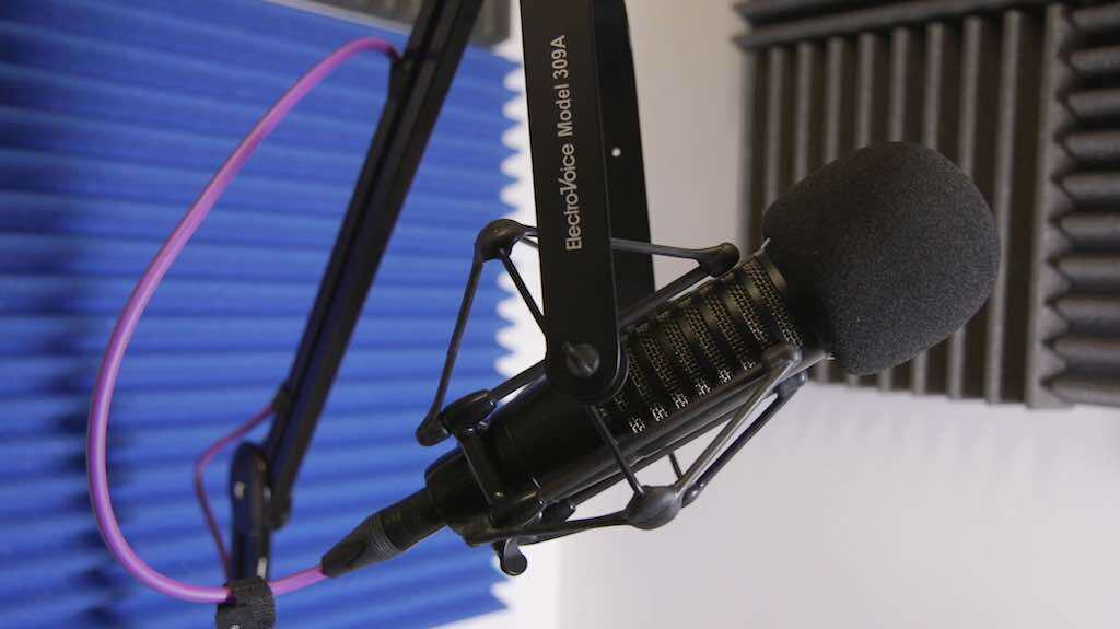 This is an image of the Electro Voice 309A Shock Mount with a black mic attached. The backdrop is a blue sound panel.