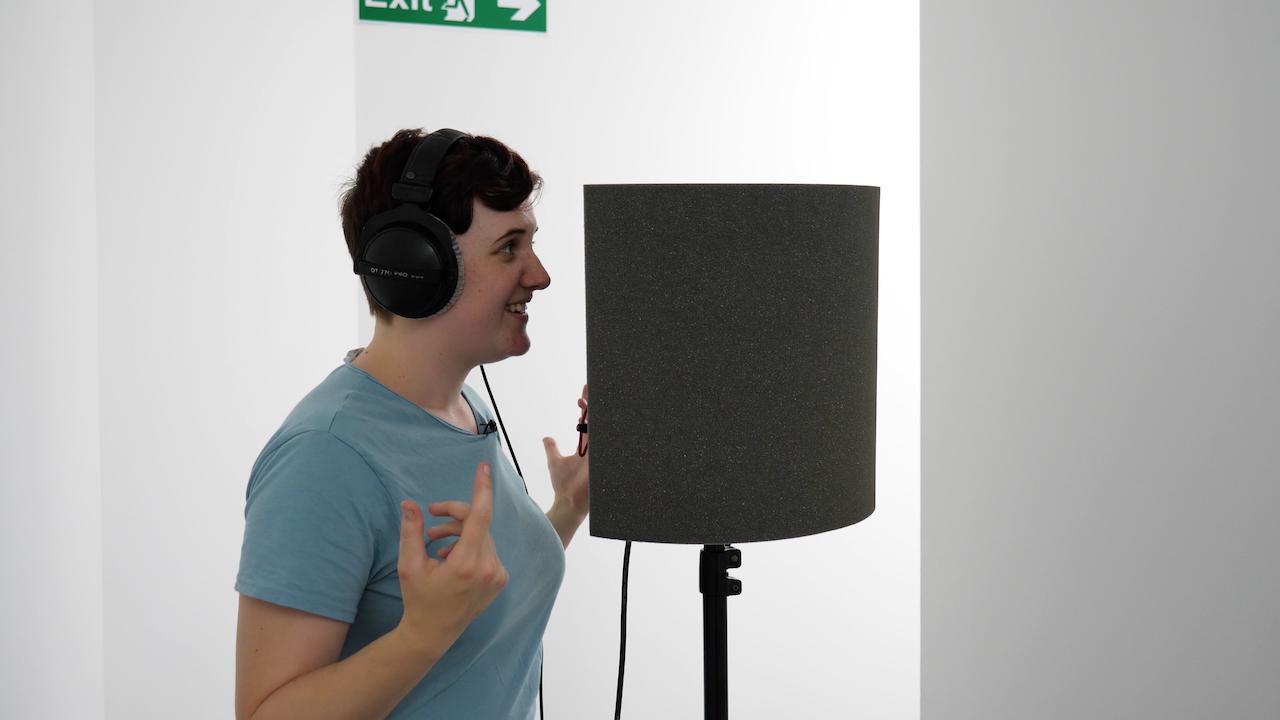 Image shows a woman speaking into a mic which has the Pro Acoustic Foam Microphone Screen around it.