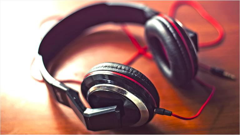 The backdrop is dark reddy brown. In the centre of the image is a pair of black headphones and the red wire is underneath it.