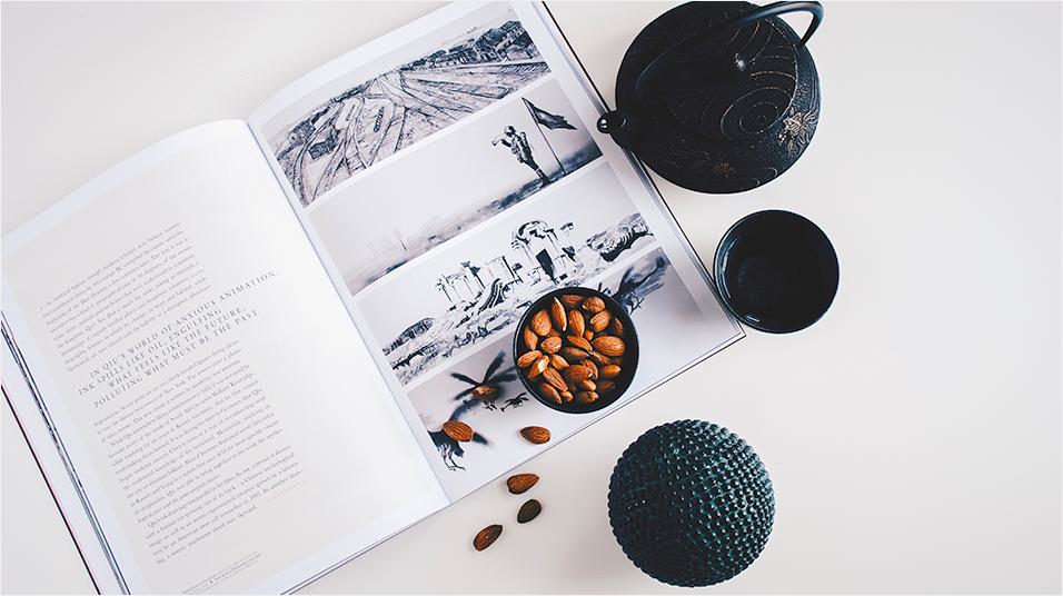 This is an image of a magazine open on a page with a set of illustrations on it. On the book there is a bowl filled with brown seeds. There is a traditional black tea set on the left of the book.