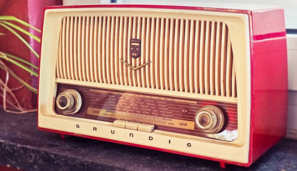 Image shows a red, retro Grundig radio on a table.