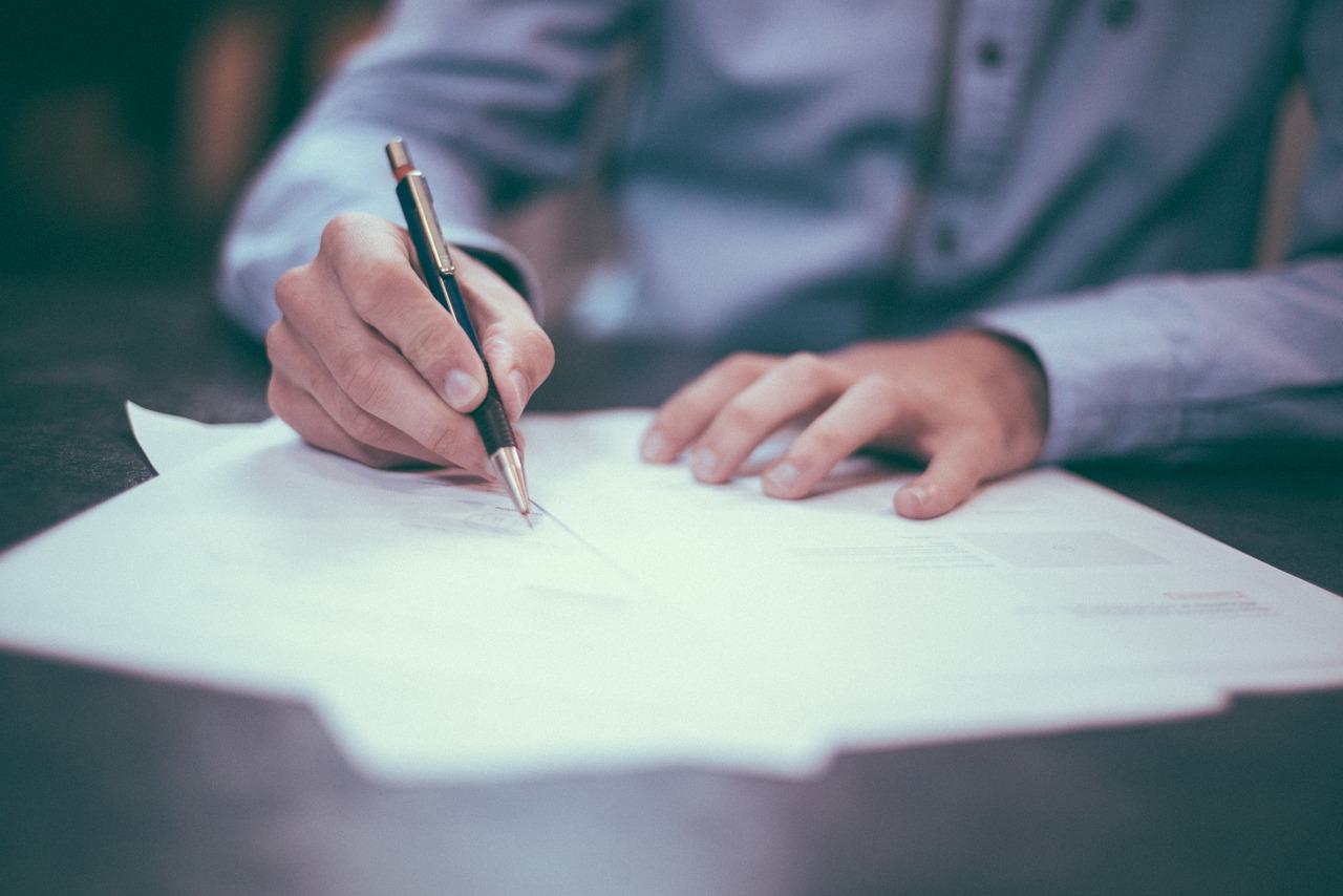 Image shows a man in a suit signing forms.