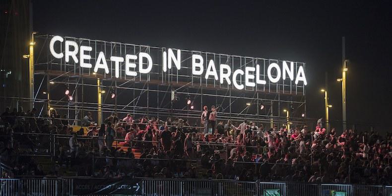 Image shows a stand of people at Primavera festival, above them is a lit up sign that reads "CREATED IN BARCELONA"