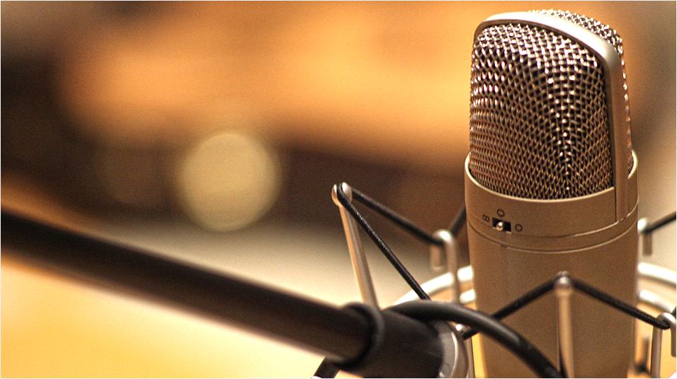 Image shows a close up shot of a silver microphone suspended from a boom arm