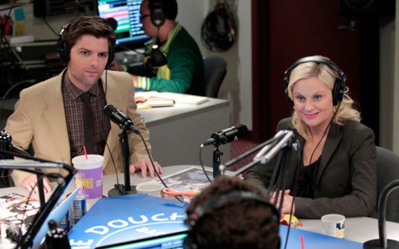 Image shows the Parks and Recreation characters Lesley and Ben being interviewed on the Crazy Ira and The Douche radio show.