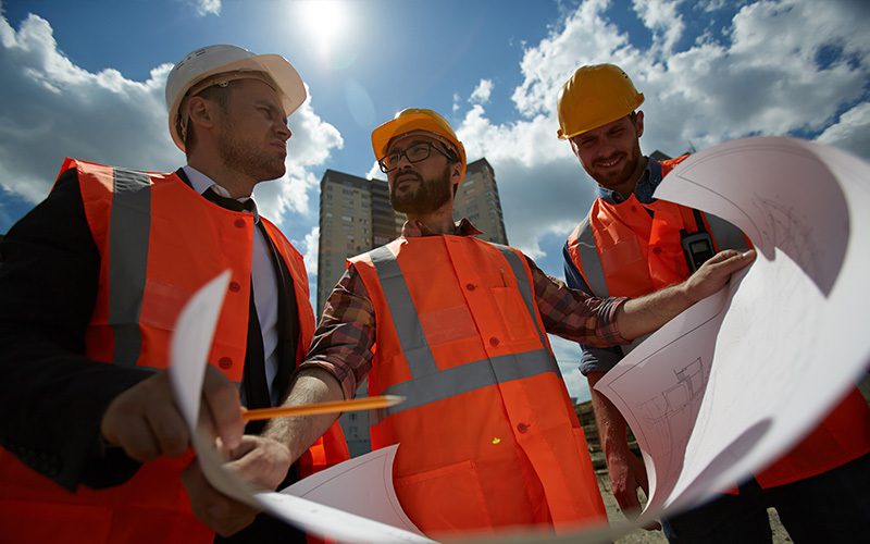 3 men review building blueprints on a construction site.