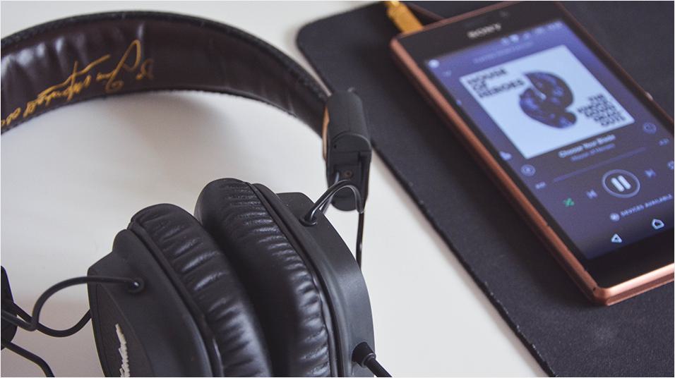 Image shows an Android phone playing music with a pair of headphones next to it, on a desk.