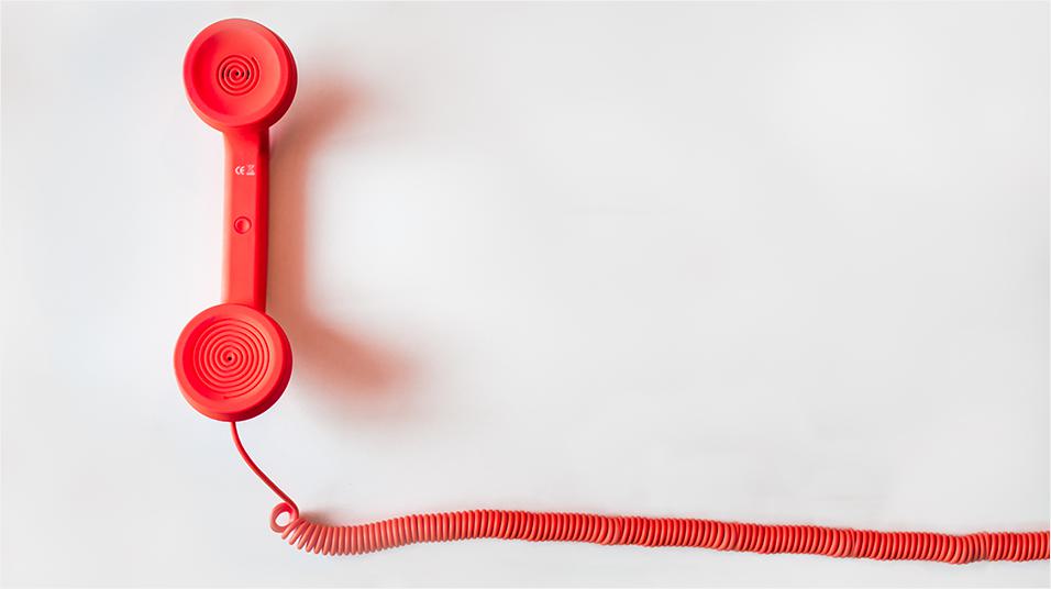 This is an image of a red telephone and corresponding spiralled wire. The phone has a shadow. This image has a neutral white backdrop.