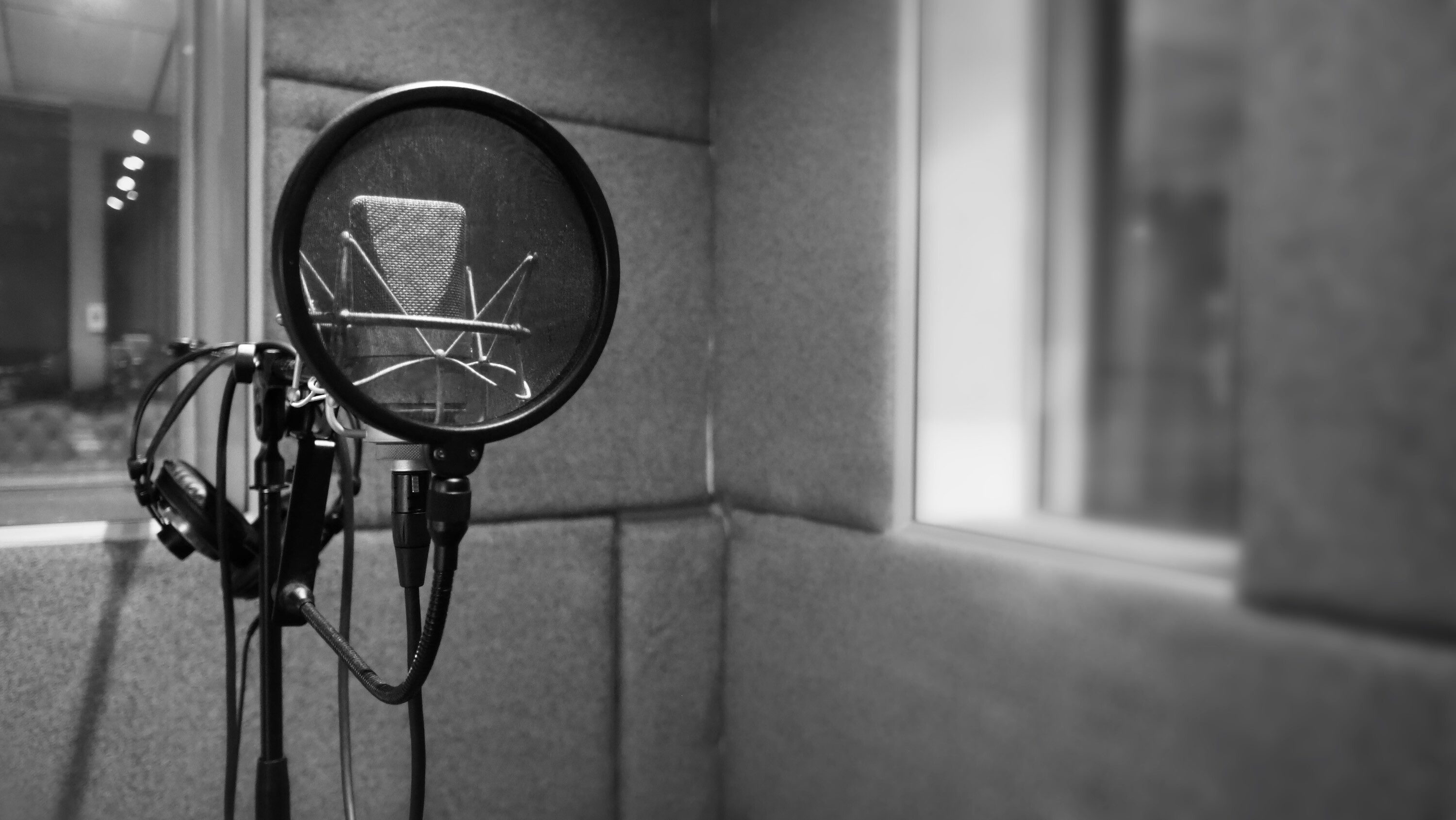Black and white image of mic on stand with pop filter inside sound booth