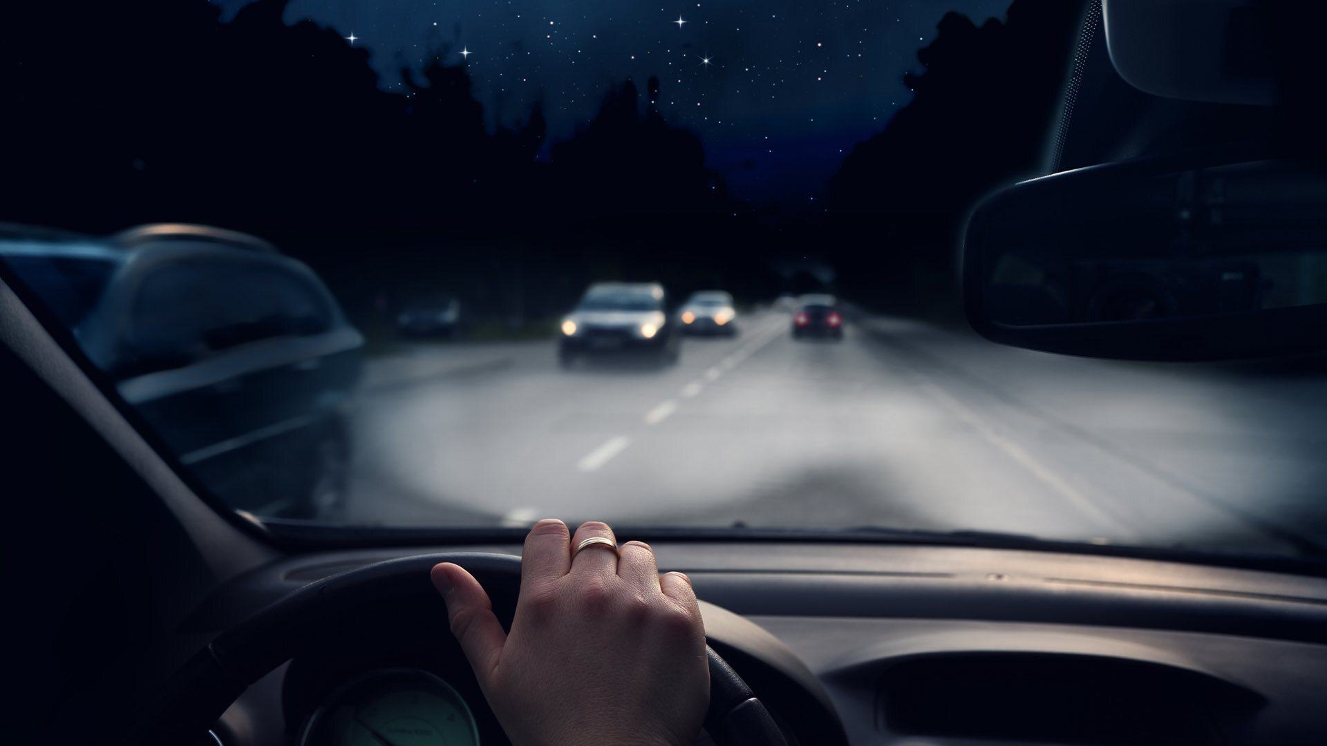 Image shows the view from a car dashboard as someone drives at night.