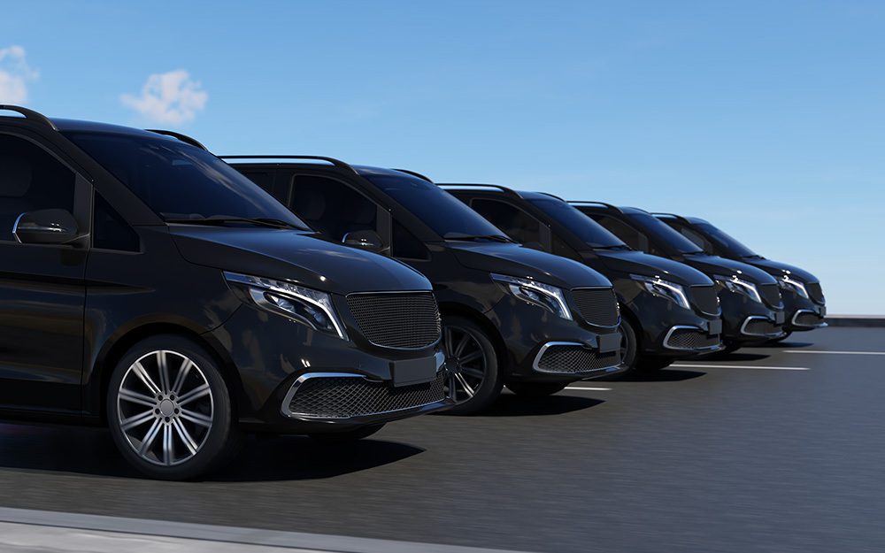 Image shows a fleet of parked, black minicabs.