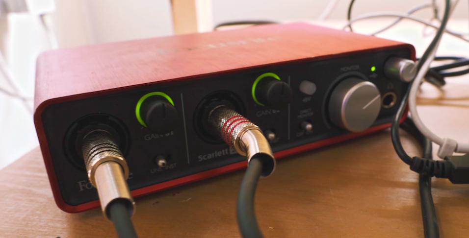 This is an image of a Focusrite 2i2 audio interface, a small red and black box with various inputs and knobs and buttons on it.