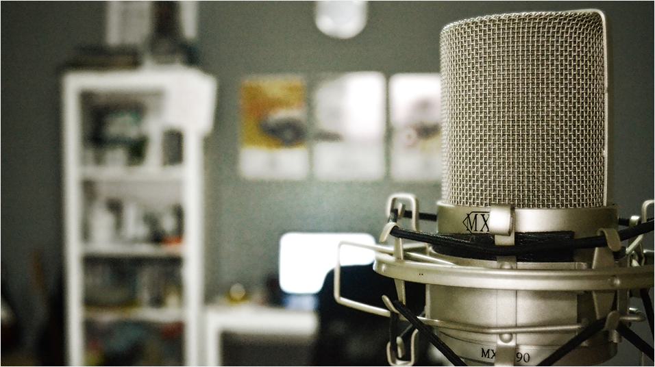 There is an olive green painted backdrop with a white bookcase visible on the left. On the right is a silver microphone zoomed in.