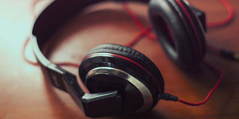 This is an image of black headphones with red wiring on a mahogany wooden table.