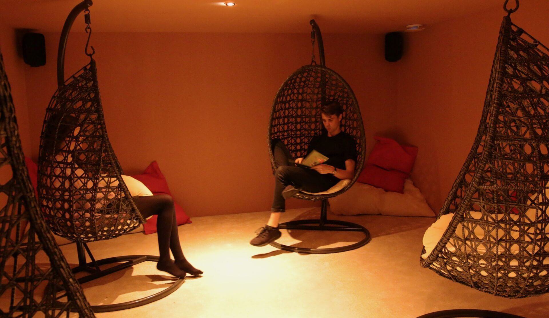 Image shows the Barbican Soundhouse shared listening space. It's a warm orange room with three egg chairs hanging from the ceilings and speakers in each corner.e