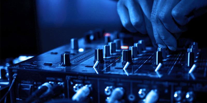 this is a dark blue image of fingers on a mixing desk. It appears to be in aclub or concert venue.