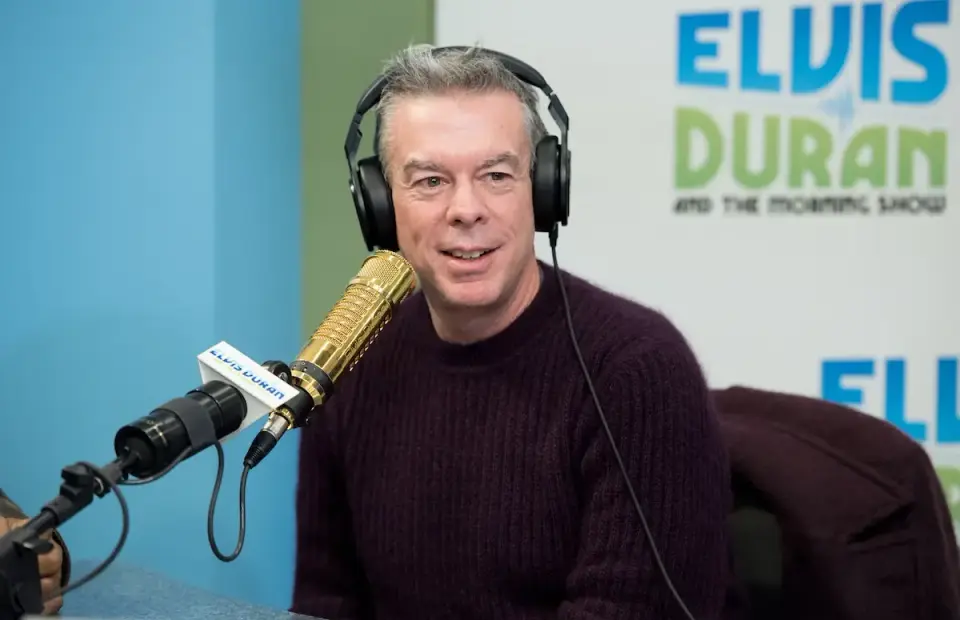 A photo of Elvis Duran behind a microphone and presenting his radio show.