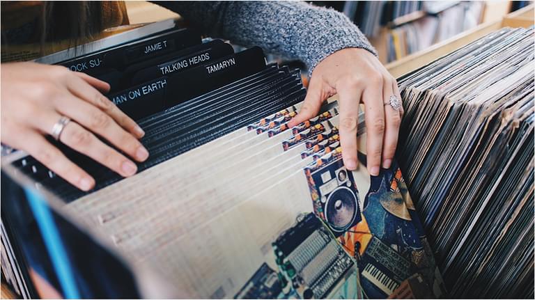 This is an image of white hands looking through vinyl records. They are resting on older ones and their fingers flick through white ones.