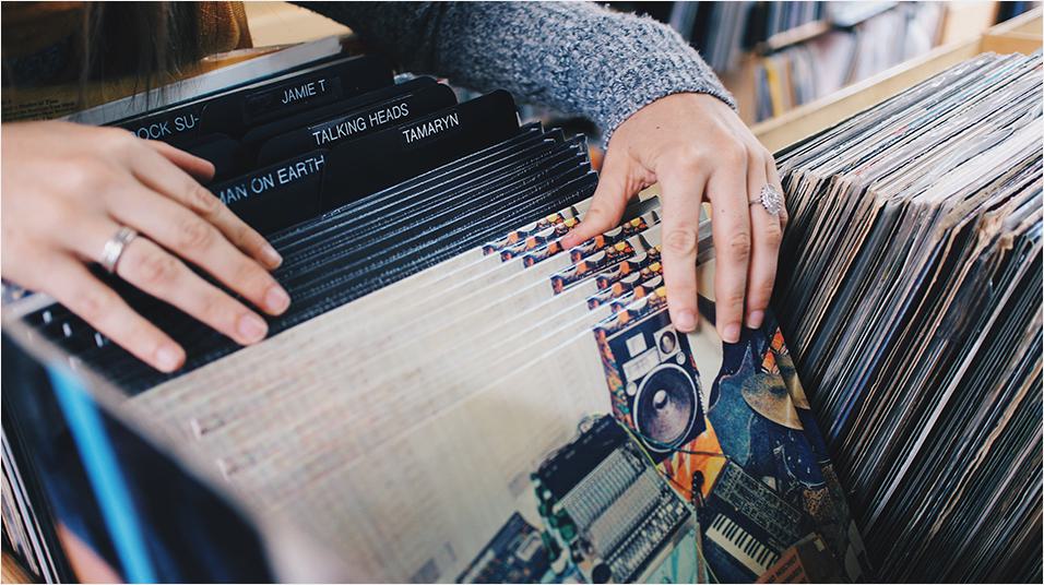 This is an image of white hands looking through vinyl records. They are resting on older ones and their fingers flick through white ones.