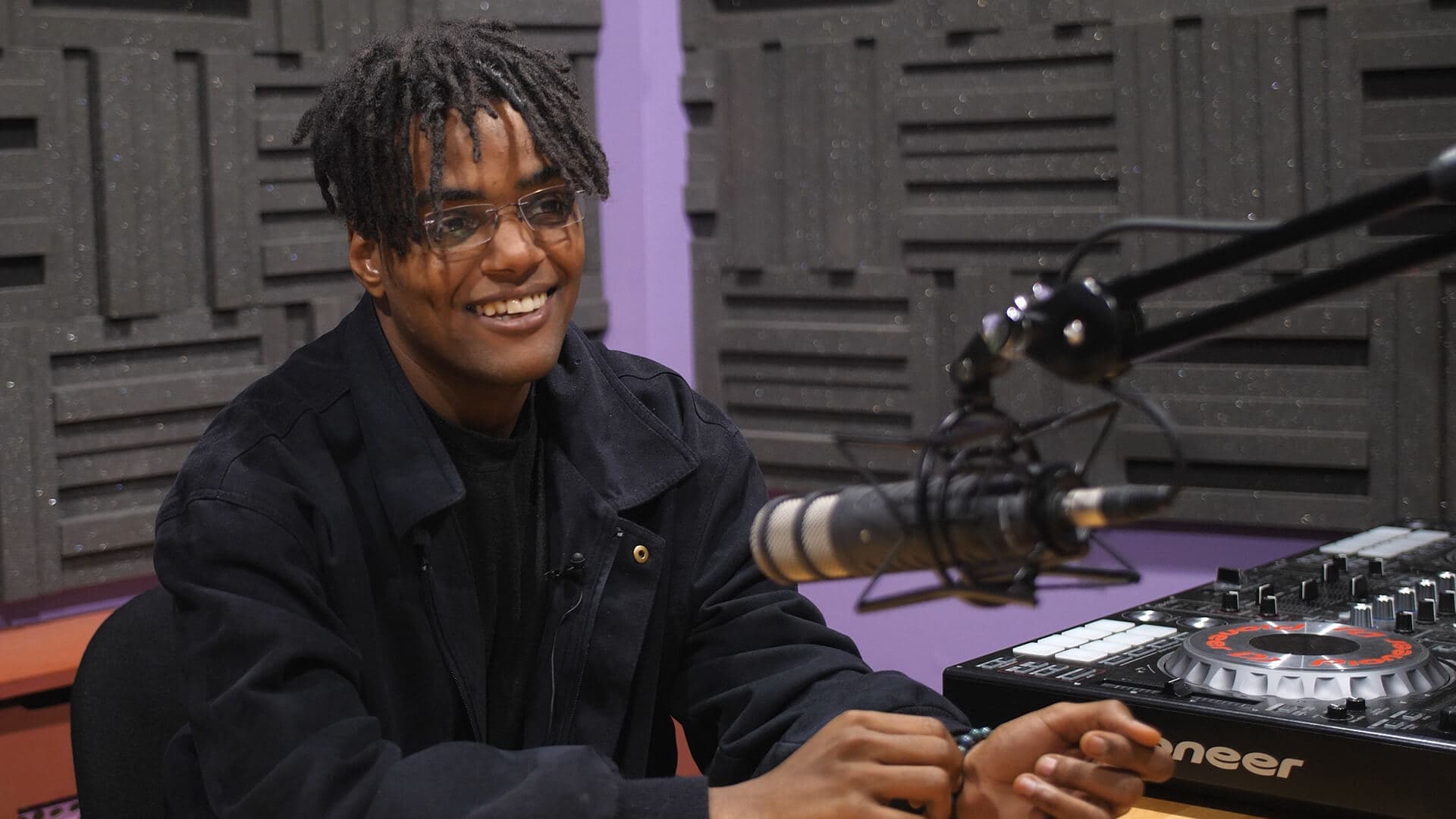 Male in a radio studio room with a mixing desk and microphone and boom arm set up.