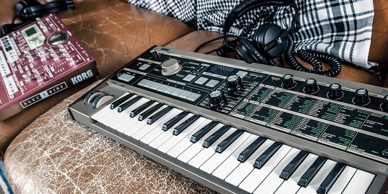 This is an image of a keyboard (black and white) on a leather brown sofa. On the left is a red mixing board with various knobs and features on it.