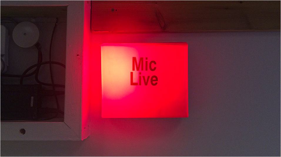 There is a bright red ON AIR box in the centre of the image. The backdrop appears to be a studio.