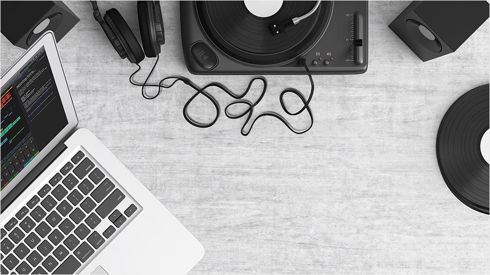 Against a grey backdrop, there is the corner of a silver Macbook on the left. On the right there is the side of a black record. In the centre there are some tangled wires.