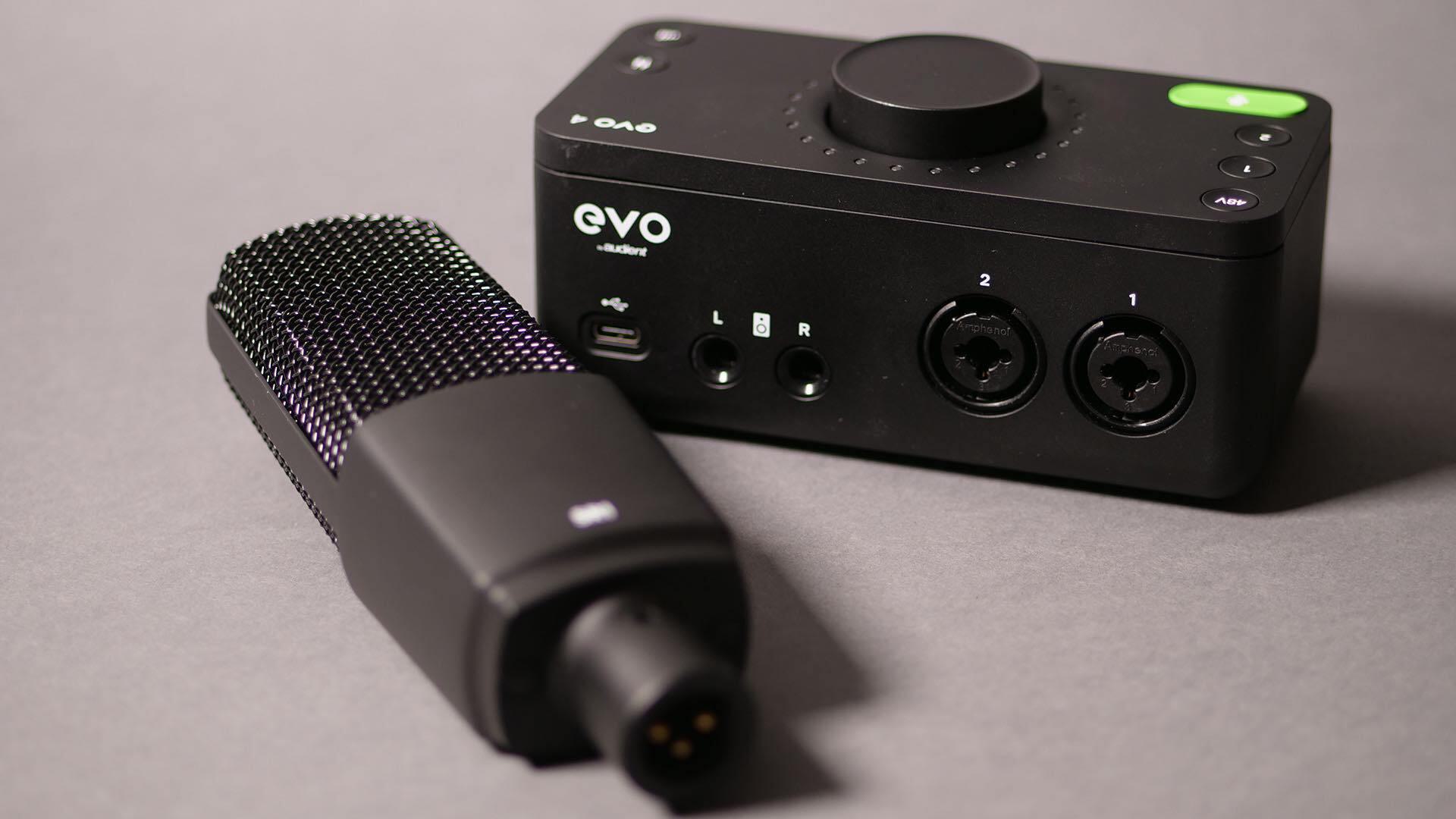 Image shows the Audient EVO SR1 microphone, on a table, next to the Audient EVO 4 interface.