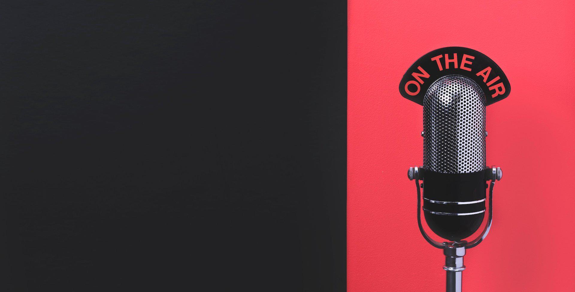 Image is a design featuring a rectangular shape which is black on the left side and red on the right. In the red section, there is an radio microphone and an 'On the air' sign perched on top of it.
