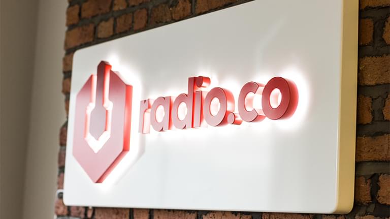 This is a neutral red bricked background with a white and red lit Radioco Sign in the centre of it.