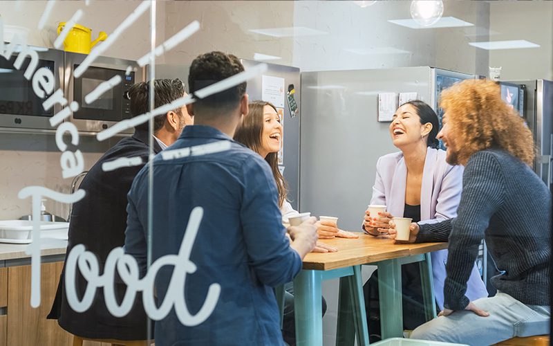 A group of colleagues sitting at a table, laughing and drinking coffee.
