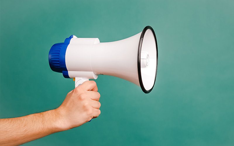 A arm holding a megaphone against a turquoise background.