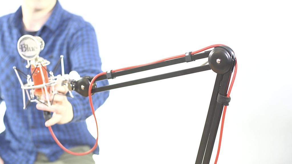 This is an image of a man in a plaid blue top and green trousers holding onto a mic attached to a Rode PSA1 Boom arm.