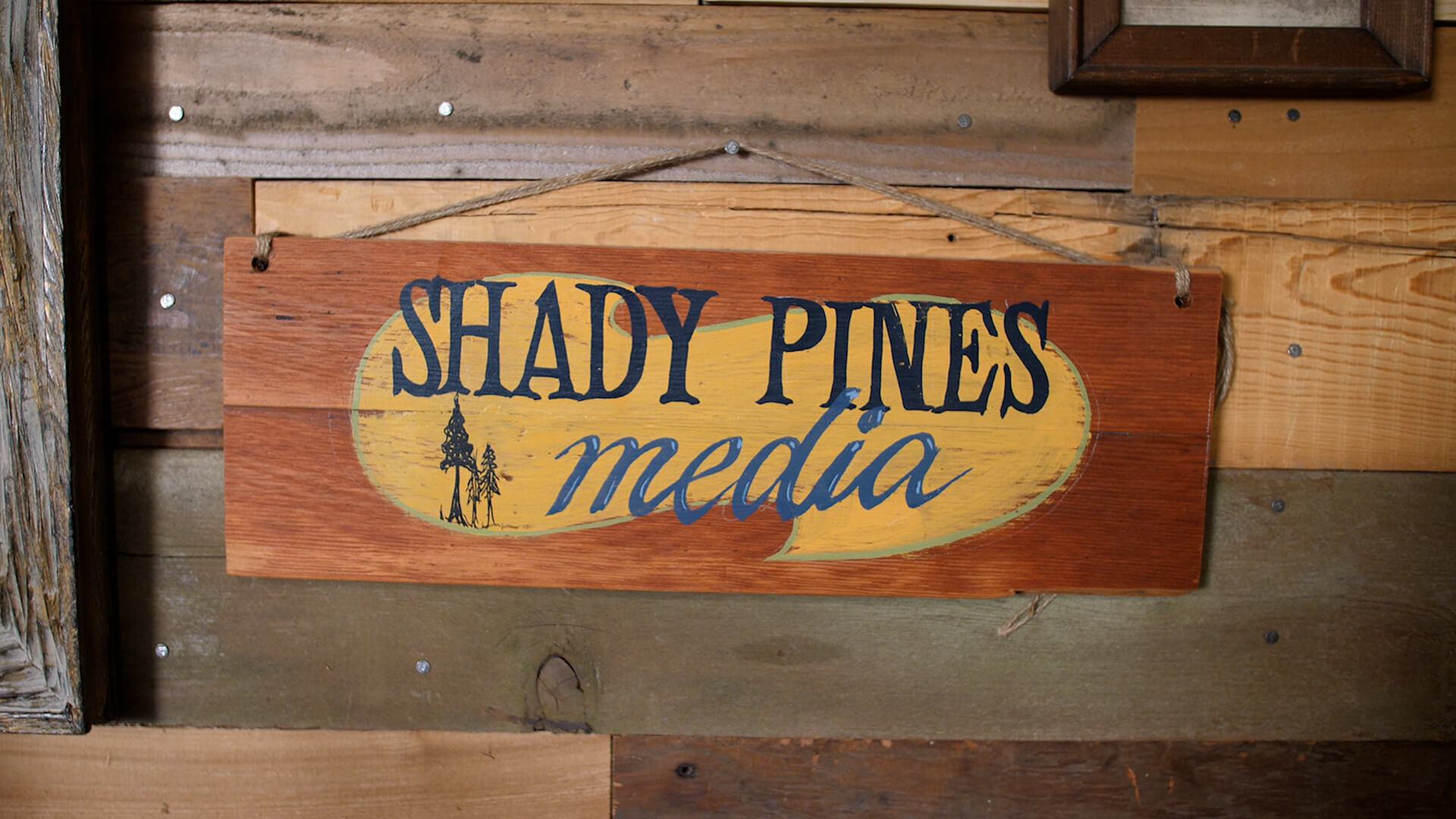 Image shows a wooden Shady Pines Media sign, nailed to a wooden plank.