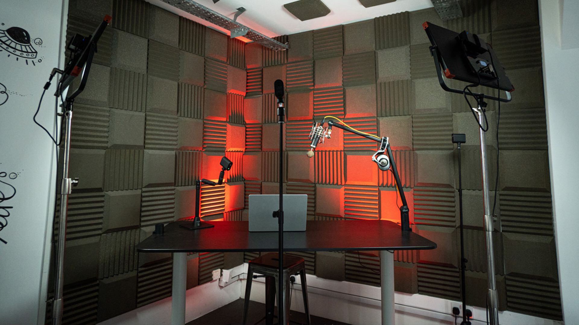 Image shows a sound-proofed studio space, with a desk, laptop, lights and some Logitech Mevo cameras set up around it.